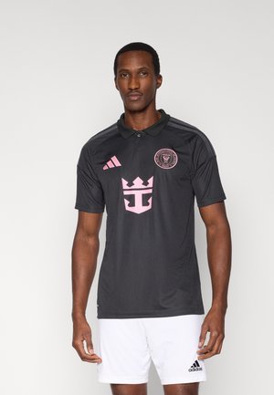 Tricou polo negru cu accente roz, cu un logo pe piept și trei dungi pe umeri. Confecționat dintr-un material neted, sportiv.