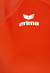 Camiseta deportiva roja con una textura suave y un tejido transpirable, con un logo blanco de "erima" destacado en el pecho.