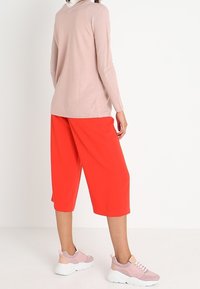 Ljust rosa långärmad topp med ett strukturerat mönster, i kombination med lösa röda culotter och rosa sneakers med vita sulor.