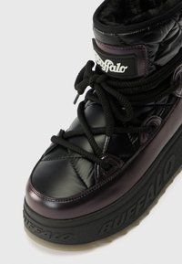 Melnas quiltētas augstas botu ar purpura akcentiem, biezs melns zole, apaļas auklas un izteikts logotipa uzlīme. Iekšpusē ir mīksta vilnas oderējums.