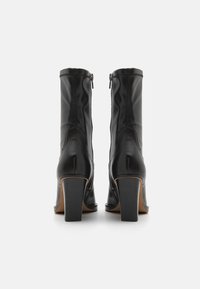 Μαύρες δερμάτινες μπότες έως τον αστράγαλο με ψηλό χοντρό τακούνι και πλαϊνό φερμουάρ, με λείο υφή και διακριτές ραφές.