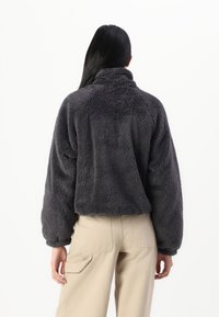 Giacca in fleece grigio scuro, corta, con collo alto, maniche puffy e superficie testurizzata, abbinata a pantaloni cargo beige.