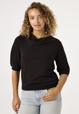 Schwarzes kurzärmliges Oberteil mit Bootsausschnitt, strukturiertem Stoff und taillierter Silhouette. Getragen mit hellblauen hochgeschnittenen Jeans.