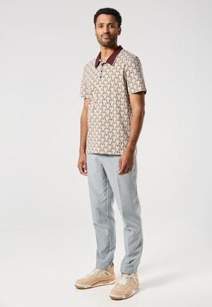 Korte mouwen polo met een hartjespatroon in beige en lichtblauw, bordeauxrode kraag, gecombineerd met lichtgrijze gestreepte broek en beige sneakers.