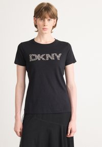 Črna bombažna majica s kratkimi rokavi in okroglim izrezom, ki na sprednji strani vsebuje besedilo "DKNY" v jasnem, okrasnem dizajnu.