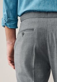 Pantalon en laine grise avec une texture subtile, doté d'une poche arrière avec bouton, accompagné d'une chemise en denim bleu.