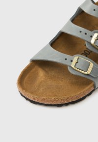 Γκρι δερμάτινο σανδάλι με τρεις ρυθμιζόμενες λουρίδες, χρυσά μεταλλικά στοιχεία και πάτο από φελλό. Υφή στη σόλα από καουτσούκ για καλύτερη πρ όσφυση και άνεση.