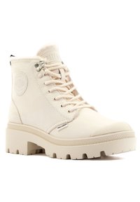 Bottine Palladium beige montante avec semelle en caoutchouc épaisse, lacets à l'avant et logo en relief sur le côté et la languette.