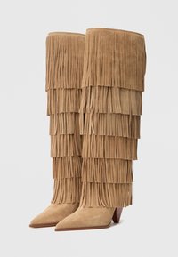Bottes en suède fauve, montant jusqu'au genou, avec un design en franges superposées, un bout pointu et un talon moyen empilé.
