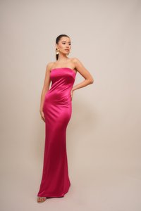 Strapless, form-fitting gown in bright pink satin. Smooth texture, floor-length design, paired with light-colored sandals and large earrings.