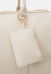 Cream-colored textured leather bag with dual handles. Features gold hardware and an attached rectangular card holder.