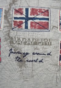 Tela gris con banderas impresas, incluyendo una en rojo, blanco y azul. Texto que dice "Viaje alrededor del mundo" en cursiva azul oscuro.