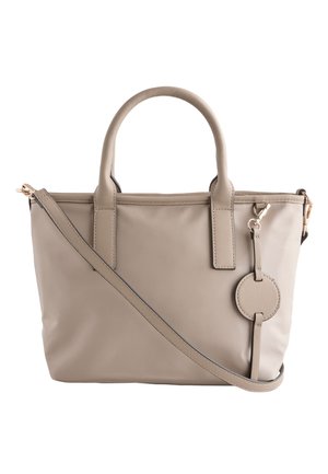 Beige tote-taske med dobbelte håndtag, aftagelig skulderrem og rundt lædermærke hængende på siden, sat mod en hvid baggrund.