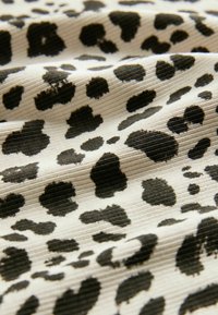 Mustekki ja beige kangas, jossa on tekstuuri pinta, esittelee leopardikuosisen kuosin, joka koostuu vaihteleva kokoisista mustista täplistä.