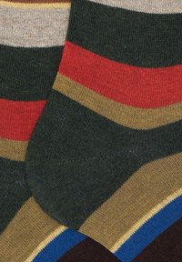 Un paio di calzini verde scuro con strisce rosse, beige e blu, caratterizzati da una visibile texture del tessuto lavorato a maglia.