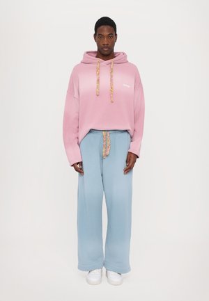 Felpa fucsia oversize con effetto sfumato, cordini con un motivo colorato, abbinata a pantaloni della tuta a gamba larga di colore blu chiaro e sneakers bianche.