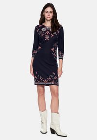 Marineblaues Kleid mit gemustertem Stickereimotiv in Rot und Weiß, dreiviertellangem Ärmel, figurbetonter Form und einem Saum oberhalb des Knies.