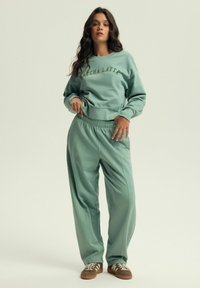 Miętowa bluza z napisem "MATCHA LATTE" oraz pasującymi dresami, z elastycznym pasem, luźnym krojem i miękką teksturą materiału.