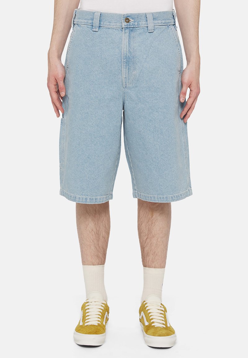 Jasnoniebieskie szorty dżinsowe o luźnym kroju, z zapięciem na guzik, pięcioma kieszeniami i prostym dołem. Noszone z żółtymi trampkami.