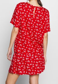 Donna che indossa un top rosso con maniche corte e una gonna abbinata con una piccola stampa floreale bianca, mostrata di spalle.