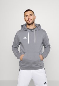 Grijze hoodie met een kangoeroezak, witte trekkoorden en een Adidas-logo op de borst. Zacht materiaal en een ontspannen pasvorm, gecombineerd met witte broek.
