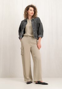 Zwarte denimjas met opgerolde mouwen, beige wijde cargobroek met zakken, en zwarte flats versierd met zilveren studs.