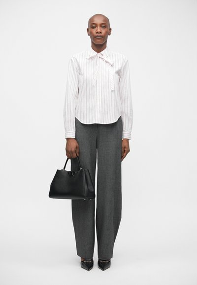 Blusa a rayas blanca y rosa con un lazo, pantalones gris ajustados y un bolso de cuero negro. Zapatos negros de punta.