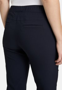 Sötétkék, rugalmas derekú nadrág sima textúrával, két hátsó zsebbel és karcsú szabással.