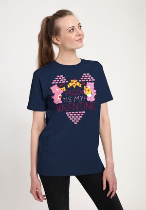 Marineblå t-shirt med pinke tegneserie-bjørne, der holder pizzastykker, med teksten "Pizza er min Valentine", sat mod et murstensmønster.
