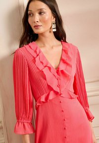 Abito rosa plissettato con scollatura e maniche arricciate, con bottoni lungo la parte anteriore e variazioni di texture in tutto l'abito.