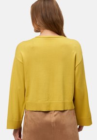 Pull en tricot jaune moutarde avec un large col, des épaules tombantes et des manches longues, présentant un ourlet côtelé et une texture.