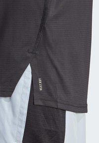 Svart idrottströja med mesh-textur, med en böjd fåll, diskret logotyp på sidan och en ljusblå underlayer synlig i botten.