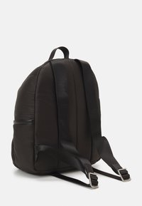Zaino nero imbottito con spallacci neri regolabili, dotato di una tasca laterale con una cerniera elegante e dettagli in metallo.