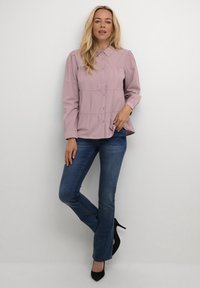 Camicia button-up di un leggero color viola con colletto, vita arricciata e maniche lunghe. Abbinata a jeans fitted di un blu scuro e tacchi alti neri.