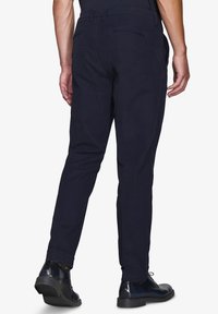 Pantaloni blu navy con vestibilità slim, dotati di passanti per la cintura, tasche laterali e una tasca sul retro. Indossati con scarpe nere stringate.
