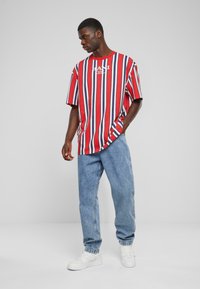 Röd och vit randig oversized t-shirt med blå detaljer, tillsammans med ljusblå denimjeans och vita sneakers, placerad avslappnat.