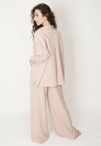 Jasnoróżowy dwuczęściowy zestaw składający się z koszuli z długim rękawem z plisą z tyłu oraz luźnych, szerokich spodni, wykonany z gładkiego materiału.