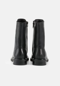 Stivaletti neri in pelle con una texture liscia, chiusura con zip e punta rotonda. Presentano una suola piatta in gomma e dettagli di cucitura minimi.