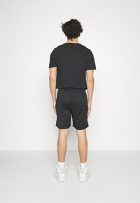 Ensemble t-shirt manches courtes et short noir, avec une coupe décontractée. Le matériau semble doux, avec une texture lisse et un design épuré.