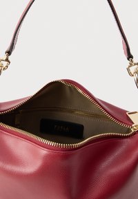 Czerwona skórzana torebka na ramię z zamkiem błyskawicznym i złotymi elementami ozdobnymi. Charakteryzuje się fakturowanym wykończeniem oraz beżową podszewką z kieszenią na zamek.