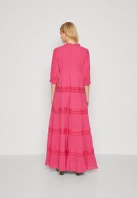 Vestido longo rosa feito de um tecido leve. Apresenta mangas bufantes, design em camadas com padrões horizontais e uma bainha com babados.