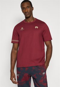 Μπλουζάκι κοντομάνικο βυσσινί από βαμβάκι, με στρογγυλή λαιμόκοψη, χρυσές λεπτομέρειες λογότυπου και άνετη εφαρμογή. Απλός σχεδιασμός χωρίς σχέδια.