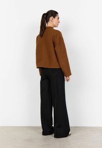 Hnedý chlpatý crop sveter s vysokým golierom, doplnený čiernymi širokými nohavicami s kontrastným prešitím. Pohľad zozadu na jednofarebnom pozadí.