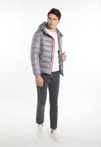 Giacca a vento grigia con cappuccio, zip frontale, dettagli rossi e blu e polsini elasticizzati. Abbinata a pantaloni grigi e sneakers bianche.
