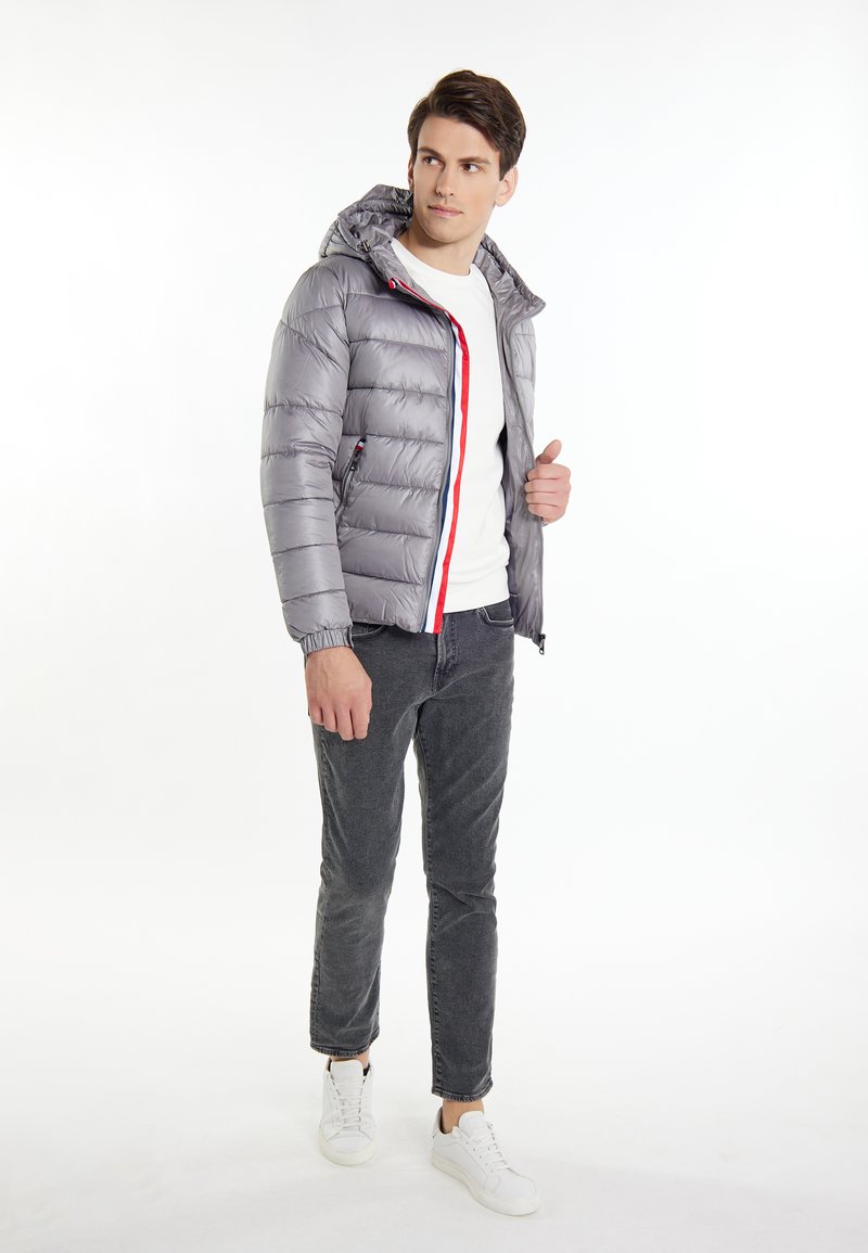 Giacca a vento grigia con cappuccio, zip frontale, dettagli rossi e blu e polsini elasticizzati. Abbinata a pantaloni grigi e sneakers bianche.