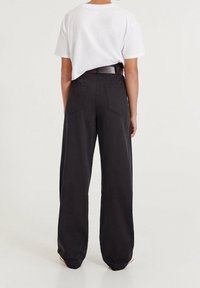 Czarne spodnie szerokie z bawełny z wysokim stanem, z dwiema tylnymi kieszeniami i paskiem. W zestawie z białą koszulą z krótkim rękawem.