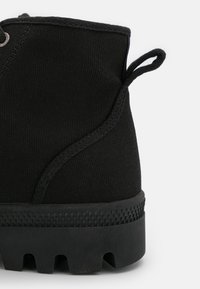 Bottine noire en toile avec une semelle en caoutchouc texturée, dotée d'une boucle à l'arrière et de coutures lisses le long des côtés.