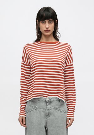 Piros-fehér csíkos hosszú ujjú pulóver kerek nyakkivágással és bő szabással, világosszürke magas derekú farmerral párosítva.