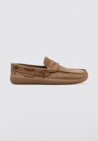 Zapato marrón de piel tipo slipper con una parte superior texturizada, acentos trenzados y suela de goma. Presenta un cordón decorativo en los laterales.