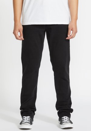 Personne portant un pantalon noir, une chemise blanche et des baskets décontractées noires et blanches, debout avec les mains détendues le long du corps.